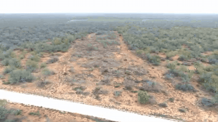 Drone flyover of a rectangular pad cleared out of dense mesquite brush, equipment parked along the caliche road